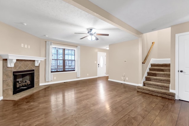 unfurnished living room with baseboards, ceiling fan, wood finished floors, stairs, and a fireplace