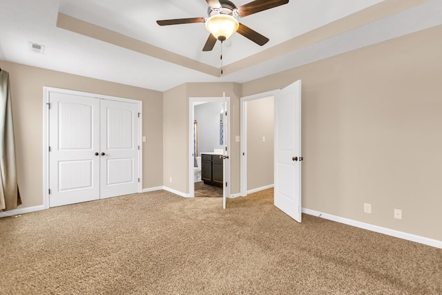 unfurnished bedroom with a tray ceiling, a closet, visible vents, carpet flooring, and baseboards