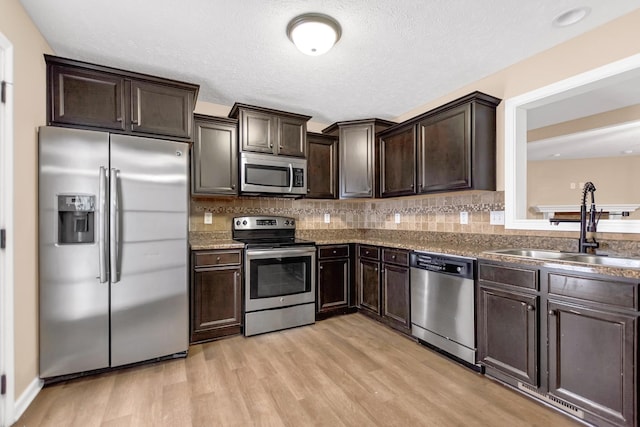 kitchen with decorative backsplash, light wood-style flooring, appliances with stainless steel finishes, dark brown cabinets, and a sink