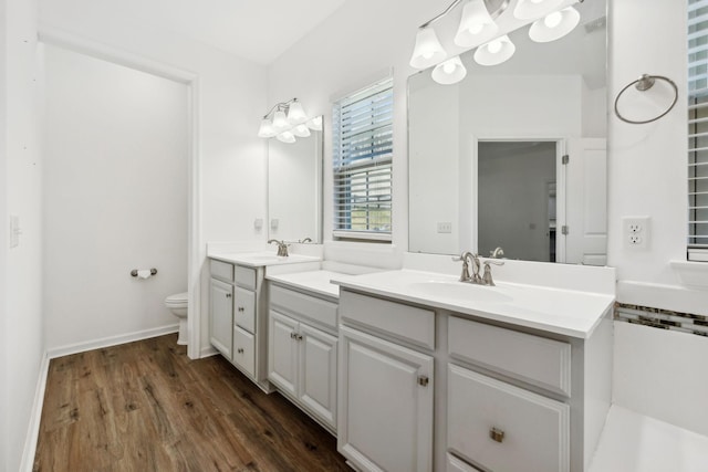 full bath featuring double vanity, a sink, toilet, and wood finished floors