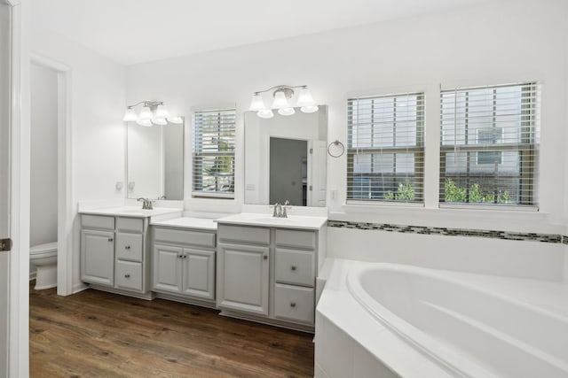 full bathroom featuring toilet, wood finished floors, vanity, and a bath