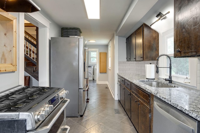 kitchen with dark brown cabinetry, appliances with stainless steel finishes, washer and clothes dryer, and a sink