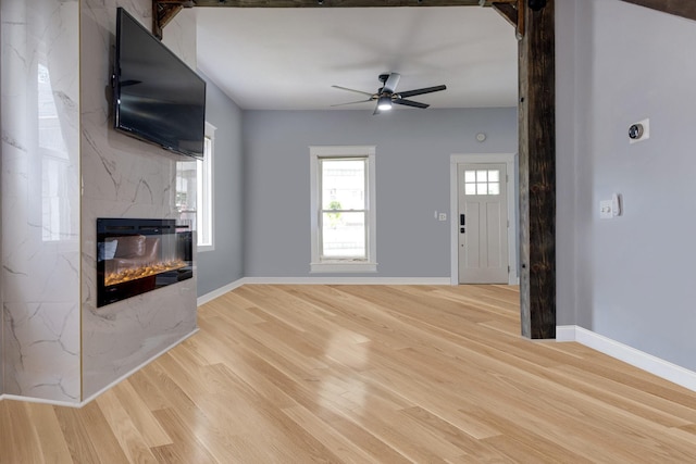 unfurnished living room featuring light wood finished floors, a premium fireplace, baseboards, and a ceiling fan