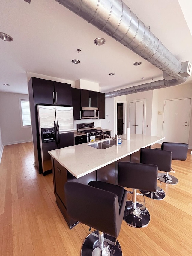 kitchen with a sink, stainless steel appliances, light wood-style floors, a breakfast bar area, and light countertops