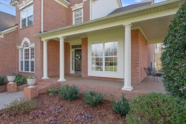 view of exterior entry featuring covered porch and brick siding