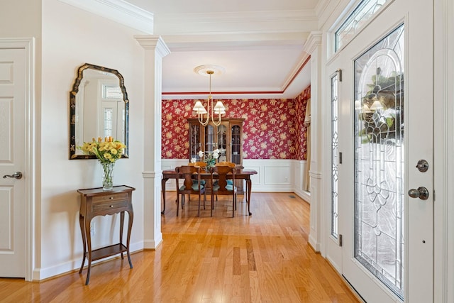 foyer entrance with a wainscoted wall, light wood-style floors, wallpapered walls, an inviting chandelier, and crown molding