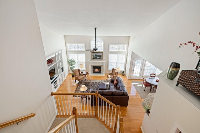 living room featuring a warm lit fireplace, a high ceiling, light wood-style flooring, and a ceiling fan