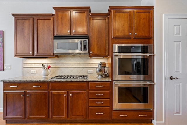 kitchen featuring appliances with stainless steel finishes, brown cabinetry, light stone counters, and tasteful backsplash