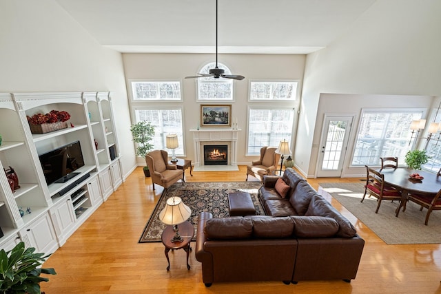 living area with light wood-style floors, a lit fireplace, and a high ceiling