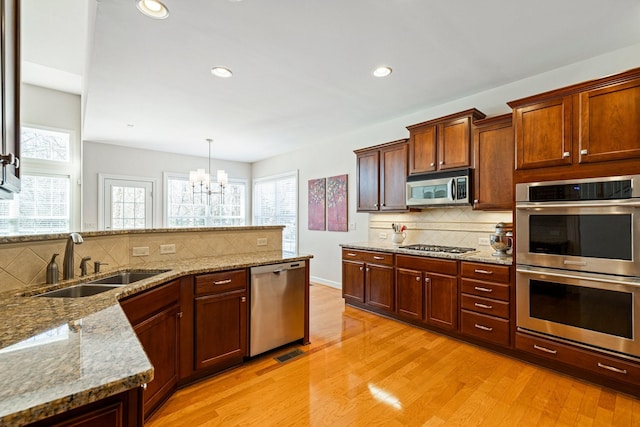 kitchen featuring light wood-style flooring, a sink, appliances with stainless steel finishes, a wealth of natural light, and light stone countertops