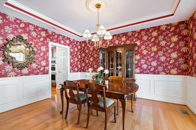 dining room featuring visible vents, an inviting chandelier, wainscoting, light wood-type flooring, and wallpapered walls