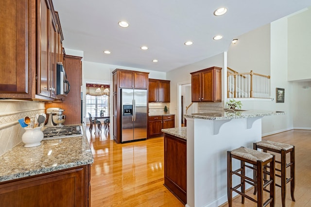 kitchen with a peninsula, stainless steel built in refrigerator, light wood-type flooring, and a breakfast bar area