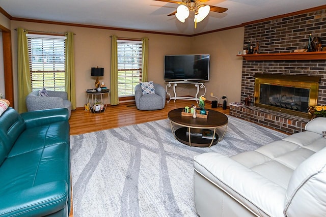 living area with a fireplace, a ceiling fan, crown molding, and wood finished floors