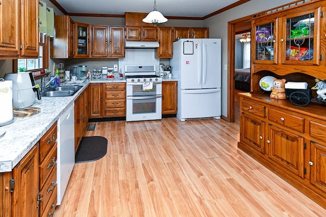 kitchen with white appliances, under cabinet range hood, brown cabinetry, and a sink