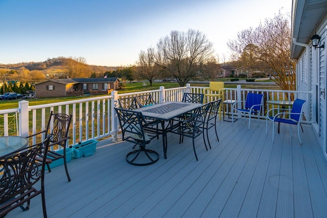 wooden deck featuring outdoor dining space, a lawn, and a mountain view