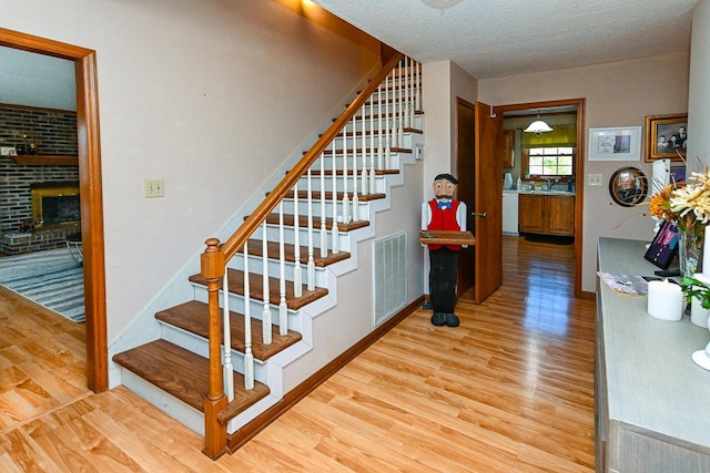 stairs featuring a textured ceiling, wood finished floors, visible vents, baseboards, and a brick fireplace