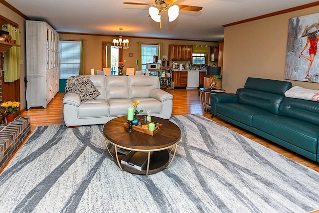 living area featuring light wood-type flooring, ornamental molding, and ceiling fan with notable chandelier