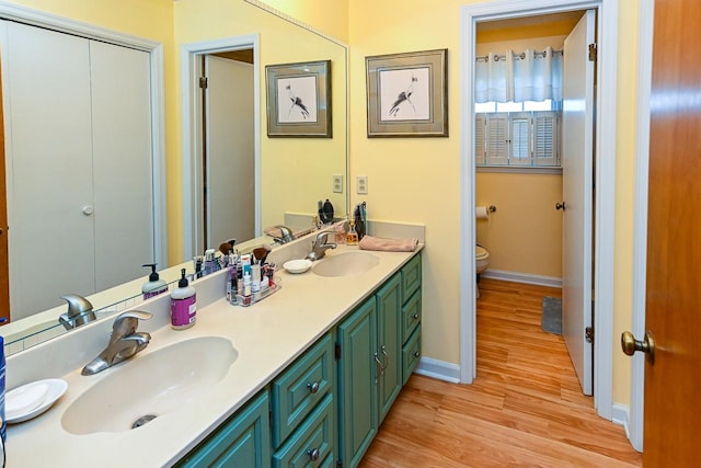 bathroom with double vanity, a sink, toilet, and wood finished floors