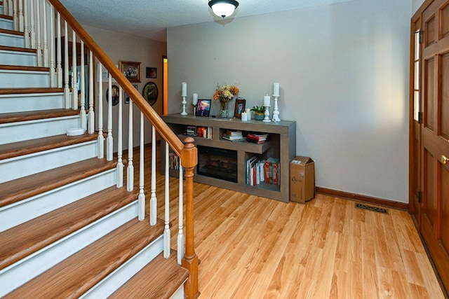 foyer entrance with visible vents, a textured ceiling, wood finished floors, baseboards, and stairs