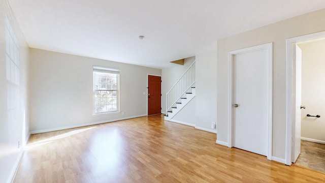 empty room featuring light wood-type flooring, stairs, and baseboards