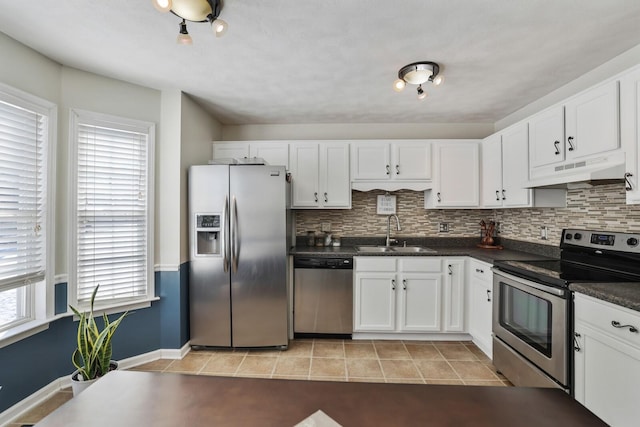 kitchen featuring light tile patterned floors, dark countertops, appliances with stainless steel finishes, a sink, and under cabinet range hood