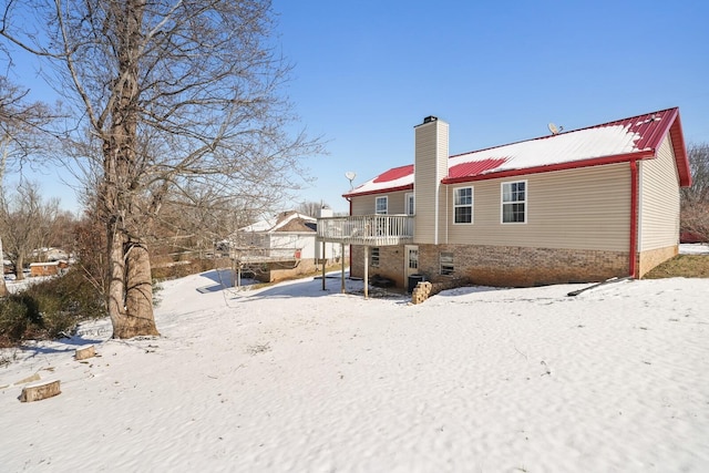 snow covered property with a deck, metal roof, and a chimney