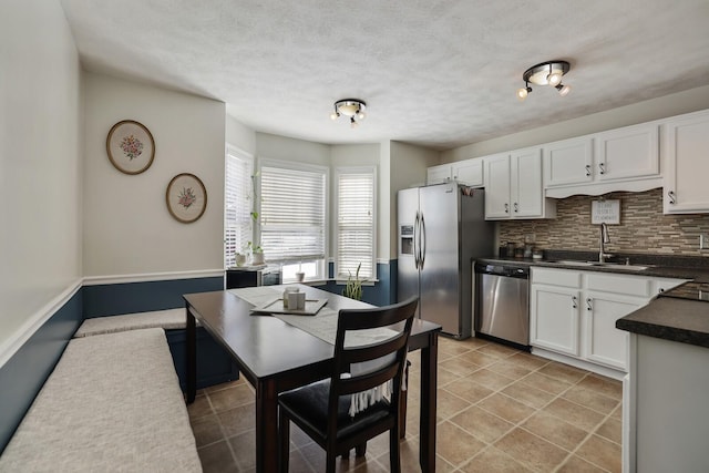 kitchen featuring stainless steel appliances, a sink, white cabinetry, backsplash, and dark countertops