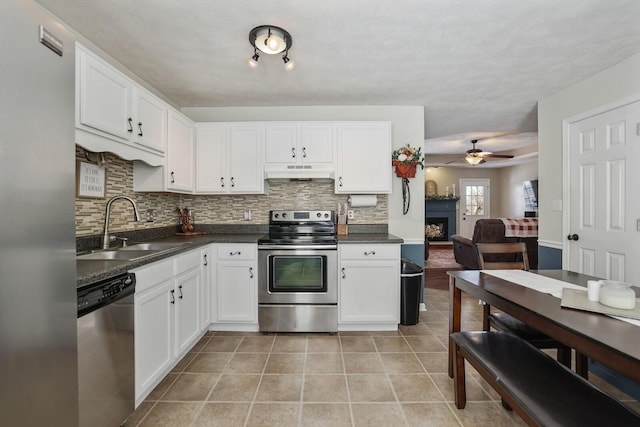 kitchen with dark countertops, appliances with stainless steel finishes, light tile patterned flooring, a sink, and under cabinet range hood