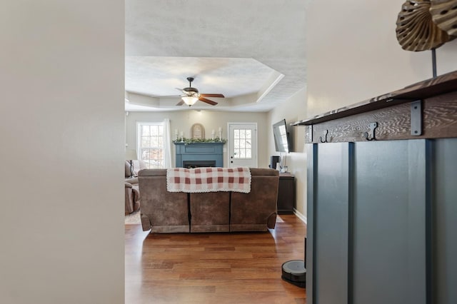 living room featuring a tray ceiling, a fireplace, wood finished floors, and a ceiling fan