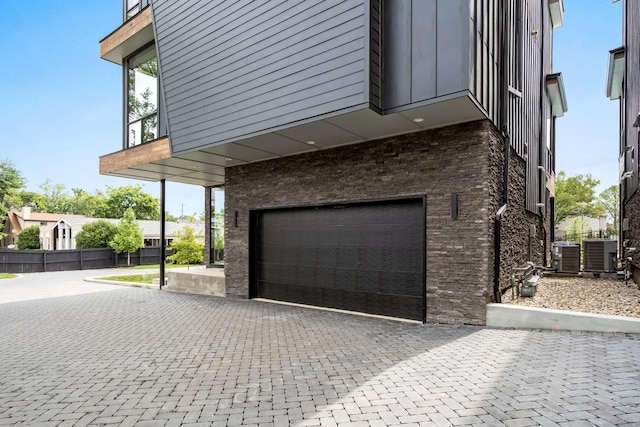 exterior space with brick siding, fence, an attached garage, and central air condition unit