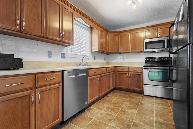 kitchen with a sink, appliances with stainless steel finishes, brown cabinetry, and light countertops