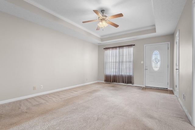 foyer featuring a raised ceiling, ornamental molding, baseboards, light colored carpet, and ceiling fan