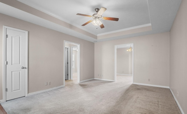 carpeted spare room featuring a tray ceiling, baseboards, ornamental molding, and a ceiling fan