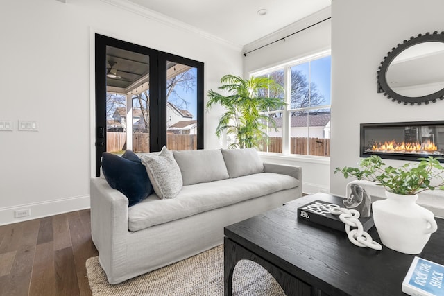 living room featuring hardwood / wood-style flooring, baseboards, ornamental molding, and a glass covered fireplace