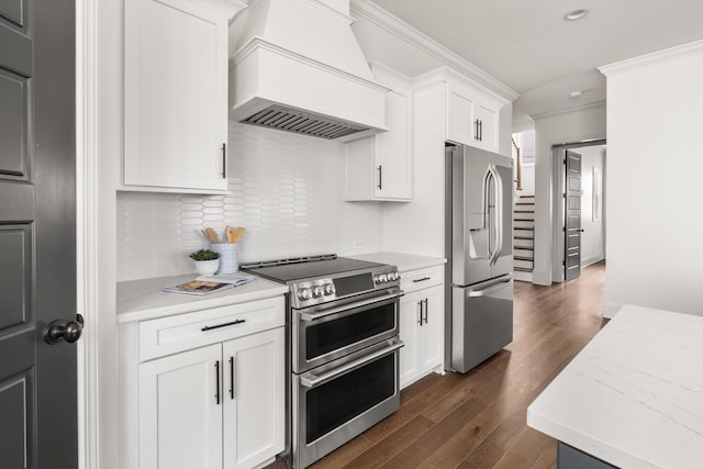 kitchen featuring appliances with stainless steel finishes, dark wood-style flooring, crown molding, premium range hood, and white cabinetry