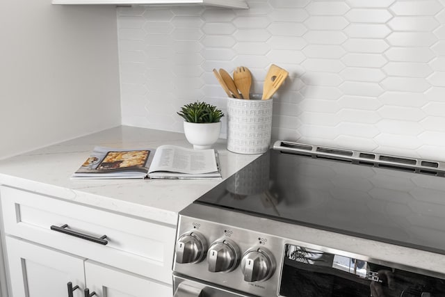 room details featuring rustic walls, white cabinets, stainless steel electric range oven, and light stone countertops