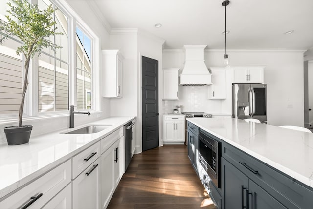 kitchen with white cabinets, custom range hood, stainless steel appliances, and a sink