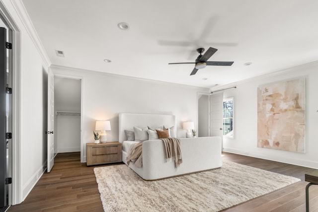 bedroom featuring dark wood-style flooring, visible vents, baseboards, a walk in closet, and crown molding