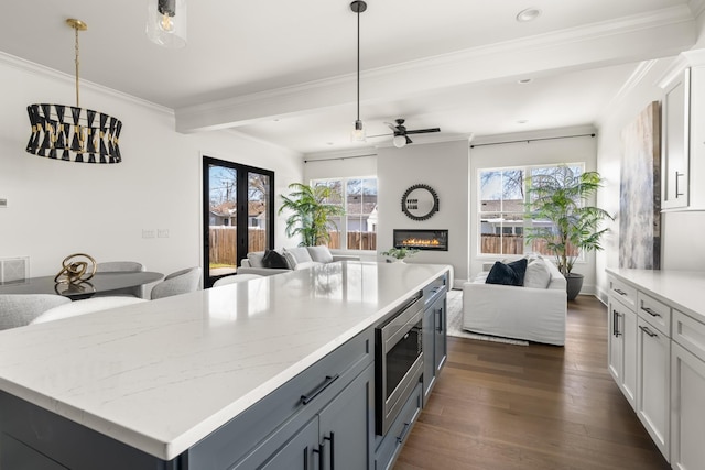 kitchen with a large fireplace, stainless steel microwave, open floor plan, dark wood-style flooring, and crown molding