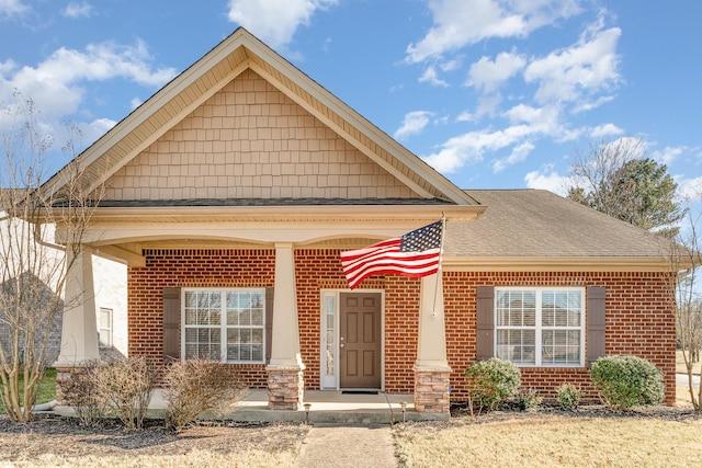 view of front of house with a porch, brick siding, and roof with shingles