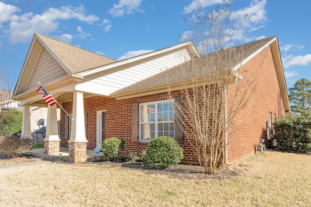 view of side of home featuring a shingled roof, covered porch, brick siding, and a lawn