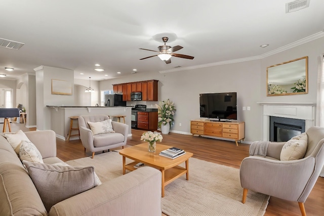 living room featuring light wood finished floors, visible vents, ornamental molding, and a glass covered fireplace