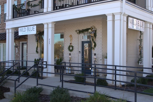 entrance to property with a porch, brick siding, and a balcony