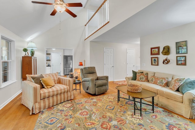 living room featuring baseboards, high vaulted ceiling, a ceiling fan, and light wood-style floors