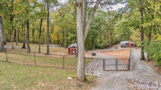 view of property's community with a lawn, fence, a wooded view, and an outbuilding