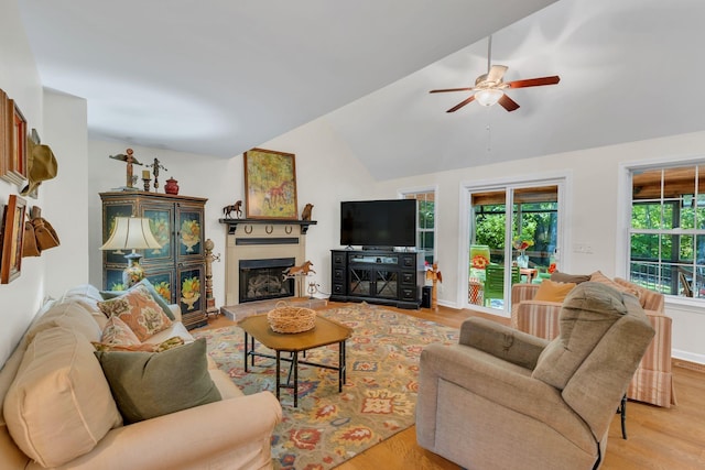 living room with a fireplace with raised hearth, vaulted ceiling, ceiling fan, light wood-type flooring, and baseboards