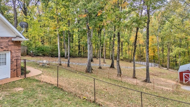 view of yard featuring a forest view, fence, a storage unit, and an outdoor structure