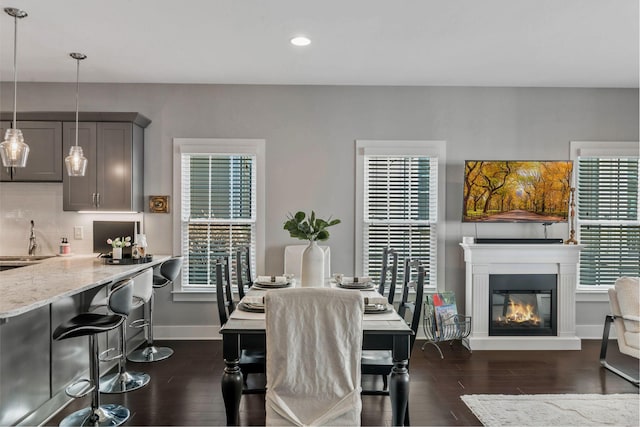 dining space with dark wood-style floors, recessed lighting, a glass covered fireplace, and baseboards