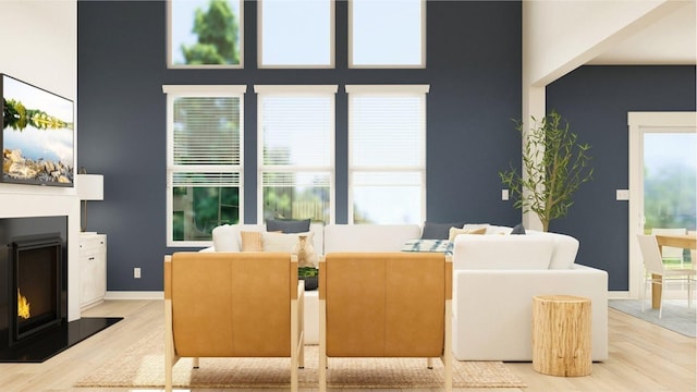 living room featuring a healthy amount of sunlight, a warm lit fireplace, a high ceiling, and light wood-style floors