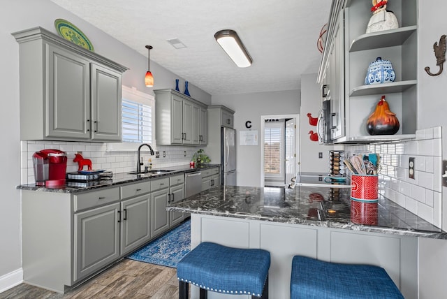 kitchen with gray cabinetry, a peninsula, wood finished floors, a sink, and appliances with stainless steel finishes